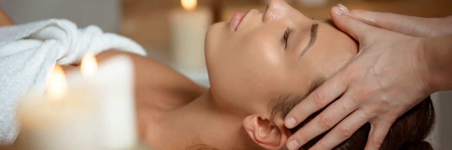 Young beautiful brunette girl having face massage relaxing in spa salon. Eyes closed. Copy space.